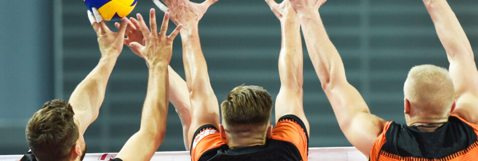 three men with lnog arms jumping in the air and blocking a volleyball