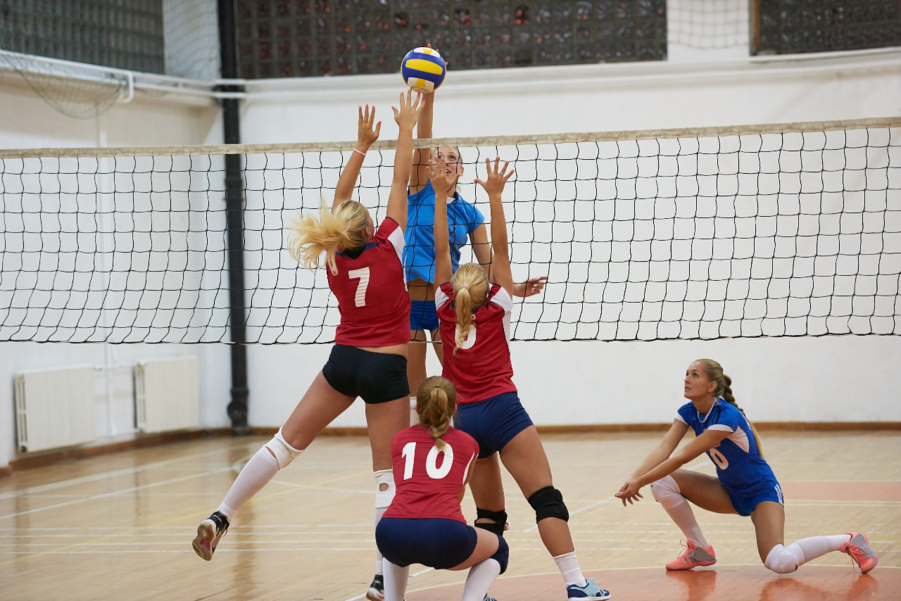 women volleyball players at the net jumping for the ball and two women covering